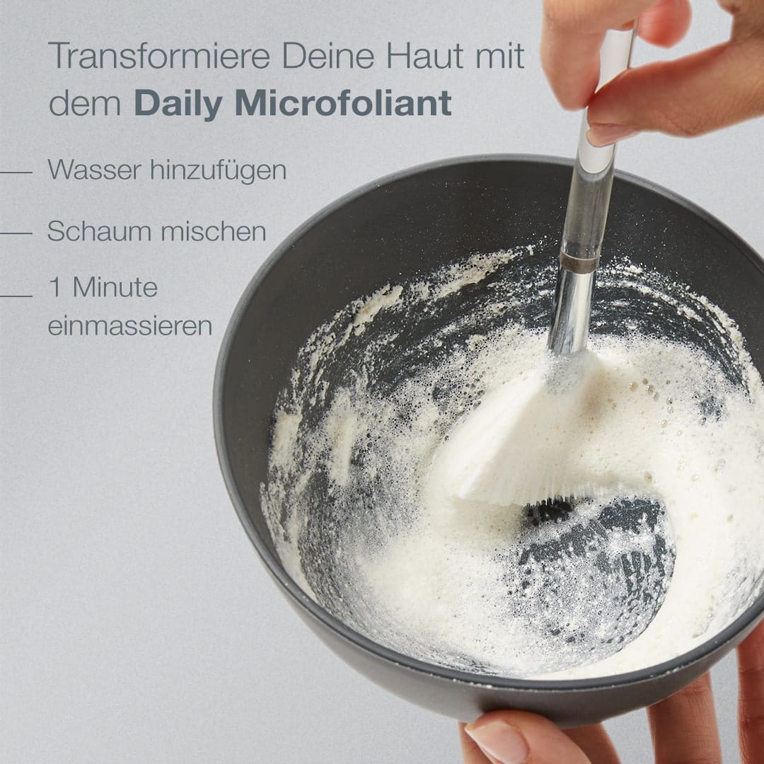 Eine Person rührt mit einem Pinsel eine Paste in einer Schüssel an, gibt Wasser hinzu, erzeugt Schaum und massiert eine Minute lang mit dem Limited Edition Smooth + Brighten Set | Daily Microfoliant mit 2 Geschenken. Dieses Produkt wird von Hautpflege-Expert:innen für ein effektives Gesichtspeeling empfohlen.